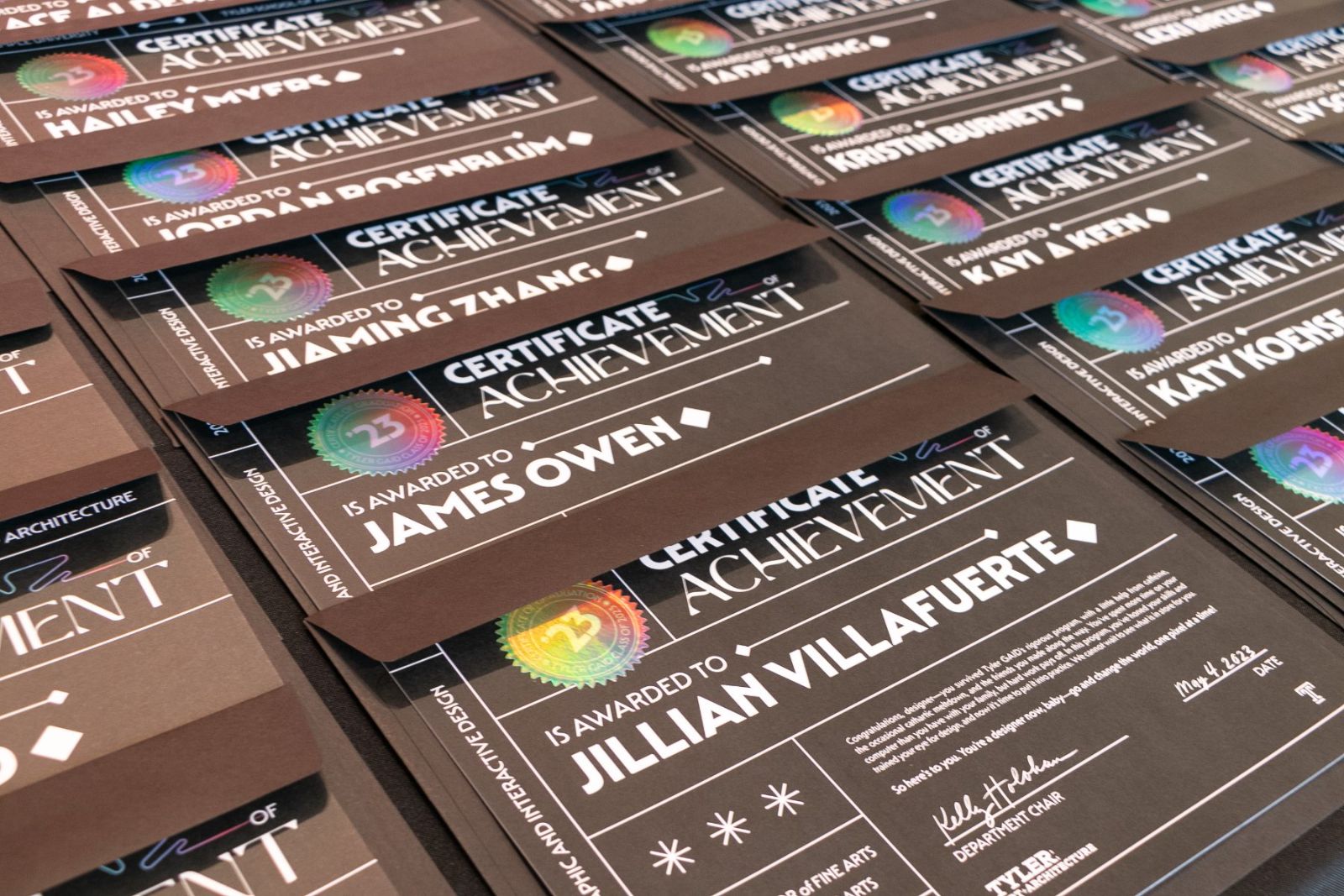 Printed certificates of achievement laid out in rows, each with a holographic class seal